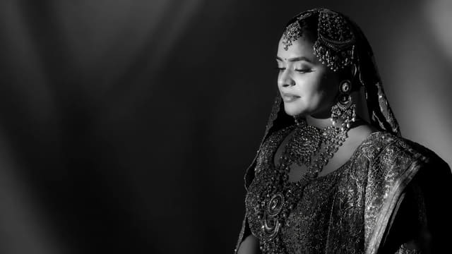 A bride in bridal jewellery — matha patti, jhumkas and a layered necklace — photographed in black and white